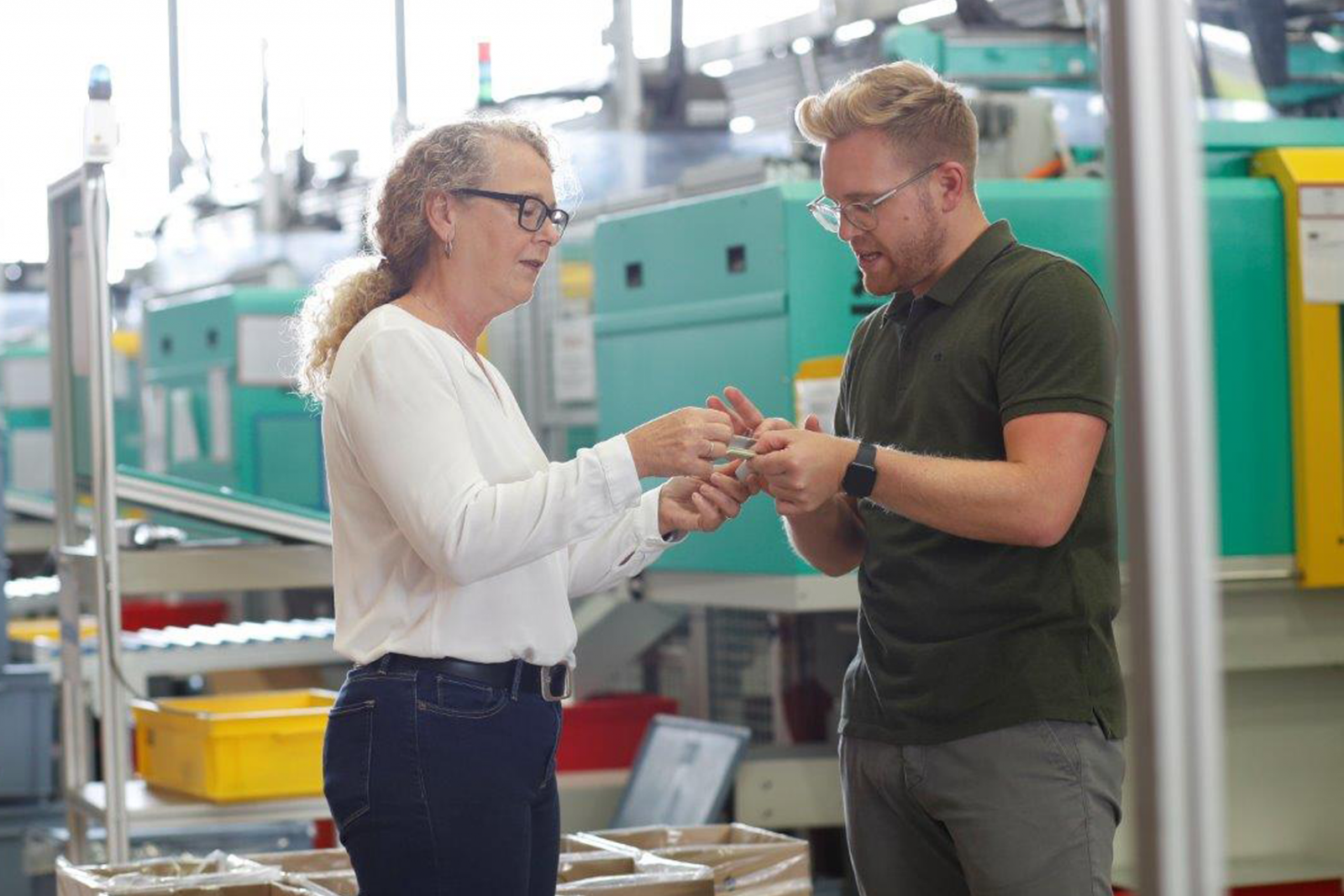 Kollegin und Kollege stehen in der Produktion und schauen sich ein Bauteil an