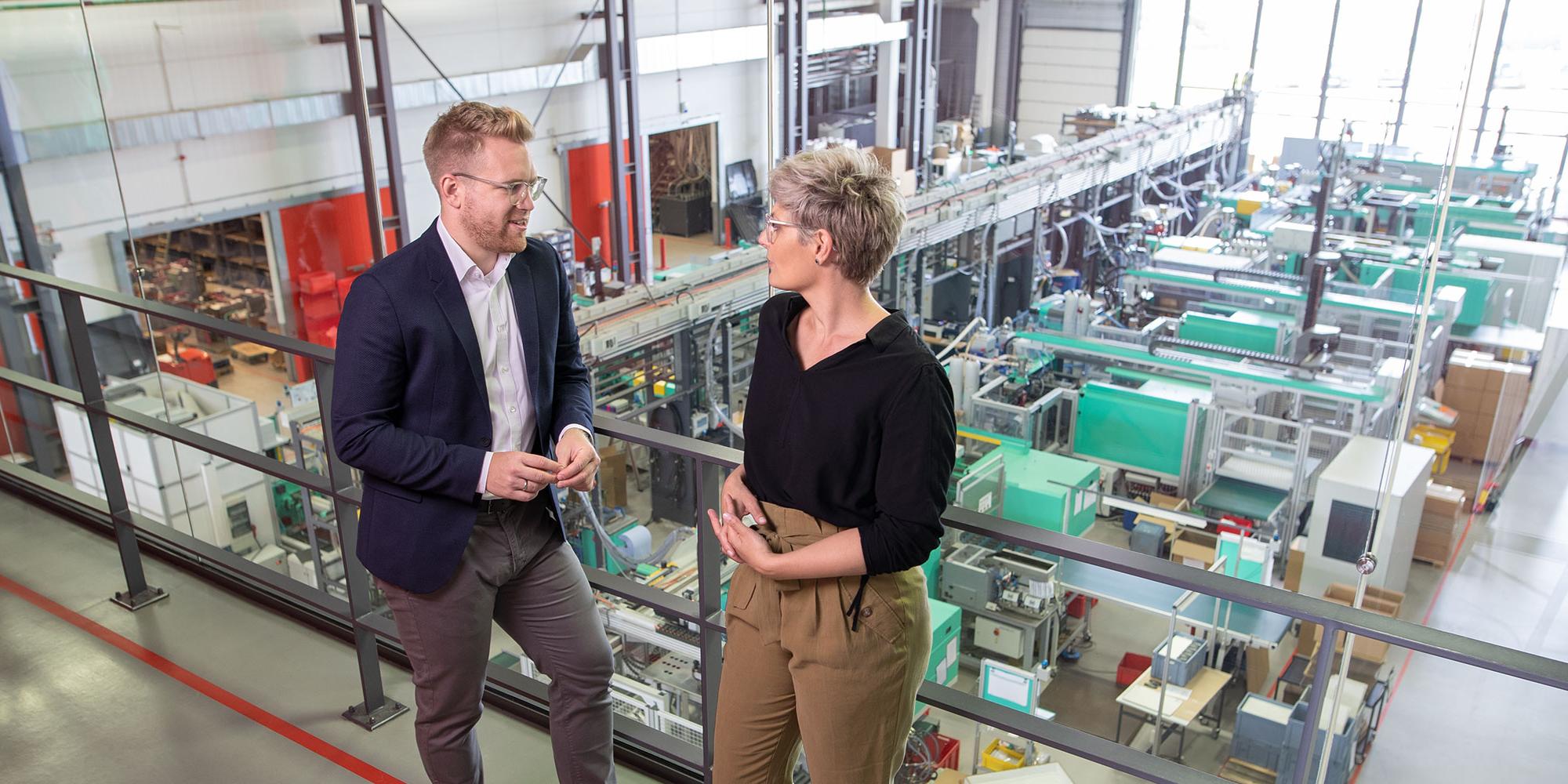 Frau und Mann auf einer Galerie im Hintergrund die Produktion