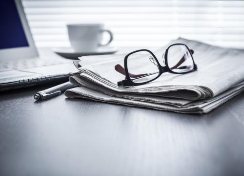 Brille auf Zeitung vor Laptop neben Stift und Kaffeetasse