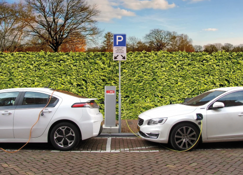 Zwei Autos an Ladestation vor grüner Hecke